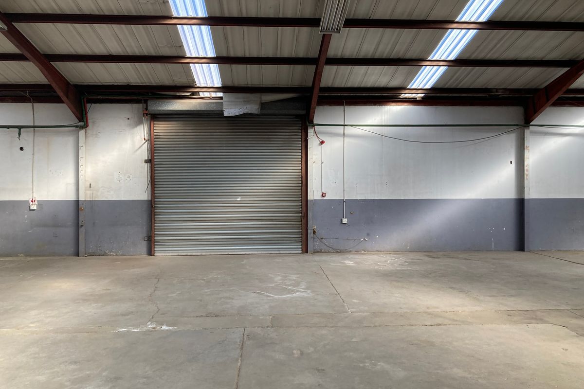 Spacious industrial warehouse unit featuring high ceilings with skylights, concrete flooring, and a large roller shutter door for easy access.