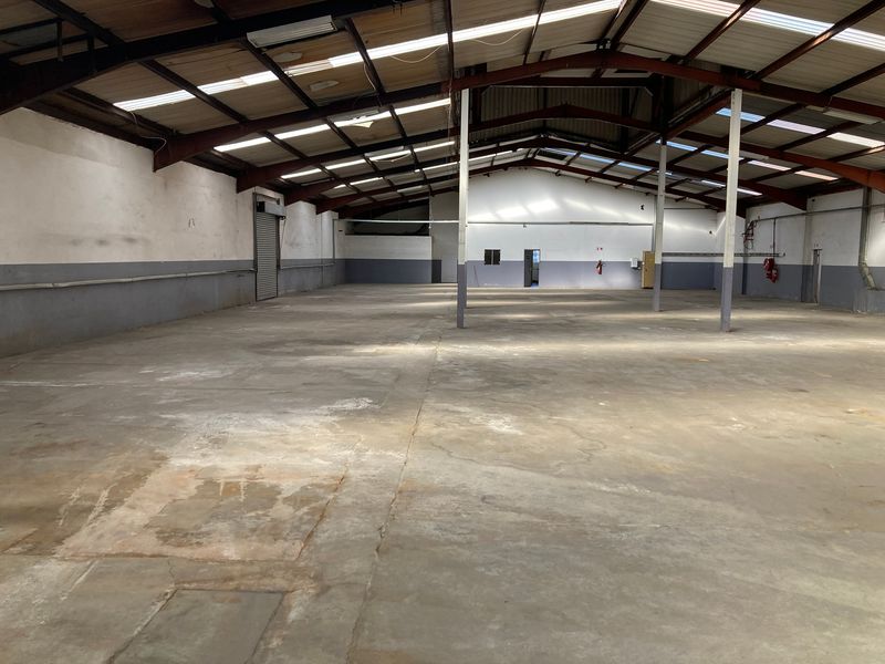 Spacious industrial warehouse unit featuring high ceilings with exposed steel trusses, concrete flooring, and a roller shutter door for easy access.