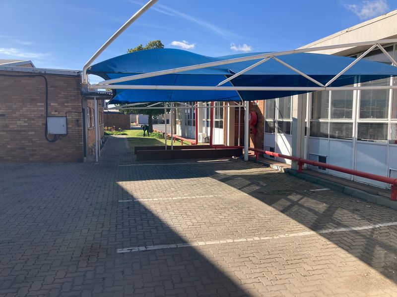 Industrial exterior area featuring a paved parking space covered by a blue shade sail structure and brick building facade.