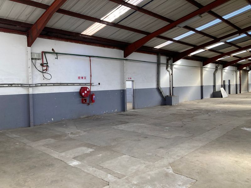 Spacious industrial warehouse unit featuring high ceilings with exposed steel trusses, skylights, concrete flooring, and essential fire safety equipment.