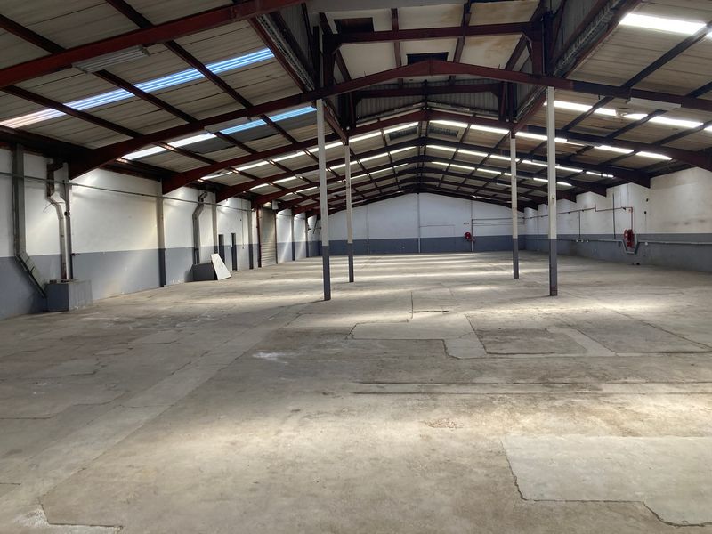 Spacious industrial warehouse featuring an exposed steel portal frame, concrete flooring, and natural light provided by translucent roof panels.