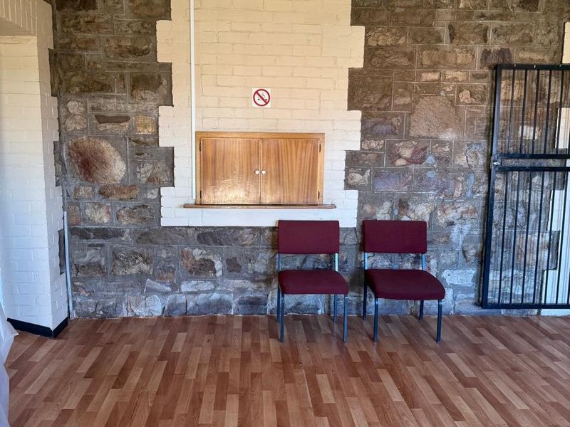 A commercial interior space featuring rustic stone masonry walls, laminate wood-look flooring, and a built-in wooden wall cabinet with a security gate.