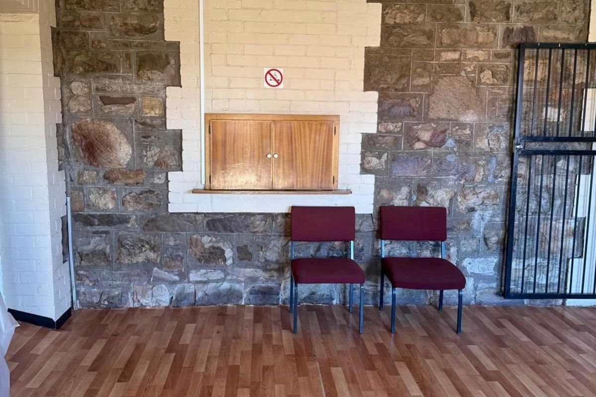 A commercial interior space featuring rustic stone masonry walls, laminate wood-look flooring, and a built-in wooden wall cabinet with a security gate.
