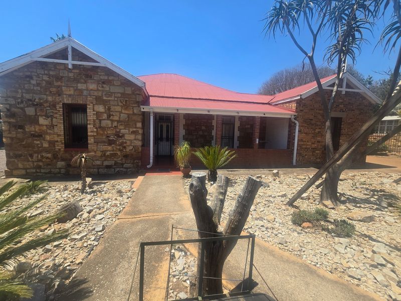 Front elevation of a commercial property featuring stone masonry walls, a red corrugated metal roof, and a covered entrance porch with security gates.