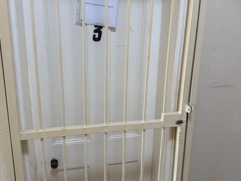 A hallway interior featuring a white panelled door secured by a metal security gate with a notice attached.