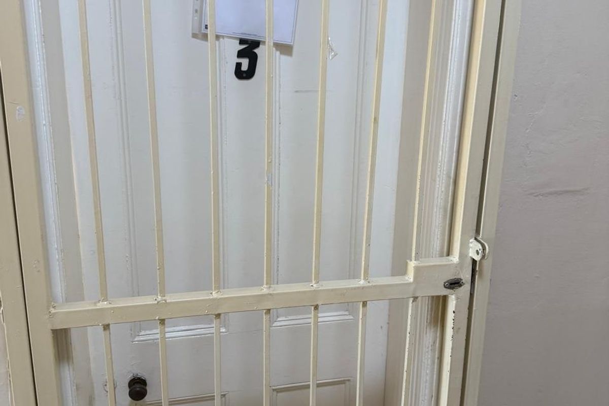 A hallway interior featuring a white panelled door secured by a metal security gate with a notice attached.