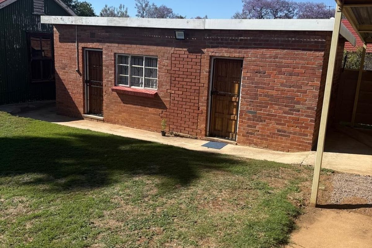 Rear view of a face brick commercial outbuilding featuring security gates and a concrete walkway adjacent to a lawn area.