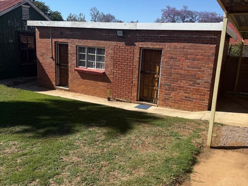Rear view of a face brick commercial outbuilding featuring security gates and a concrete walkway adjacent to a lawn area.