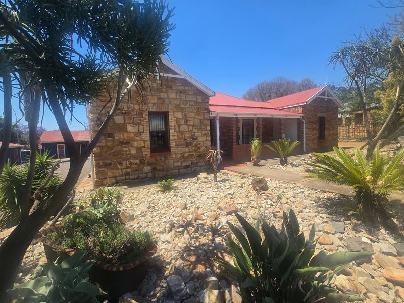 A charming commercial property featuring a stone facade, red corrugated metal roof, and a covered veranda with brick pillars.