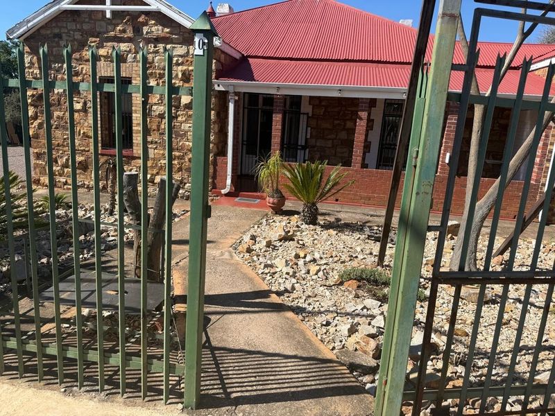 Front view of a commercial property featuring a stone facade, red corrugated metal roof, and a gated entrance with a concrete pathway.