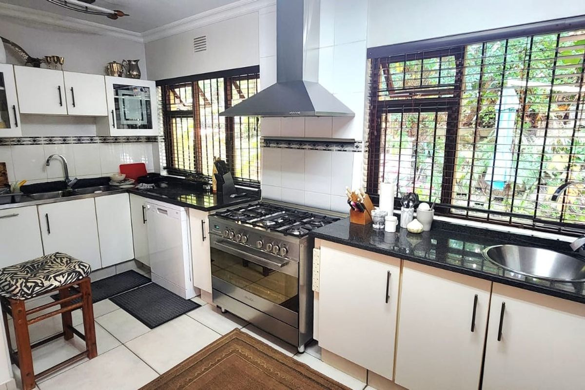 Functional kitchen featuring granite countertops, stainless steel gas stove with extractor fan, double sink, and ample built-in cabinetry with security bars on windows.