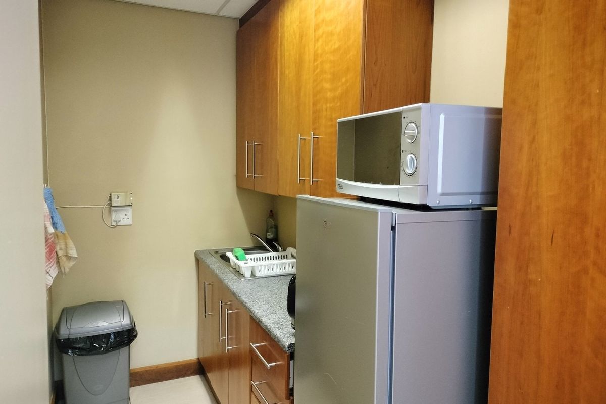 A compact kitchenette area featuring wooden cabinetry, a granite-look countertop, a stainless steel sink, and a tiled floor.