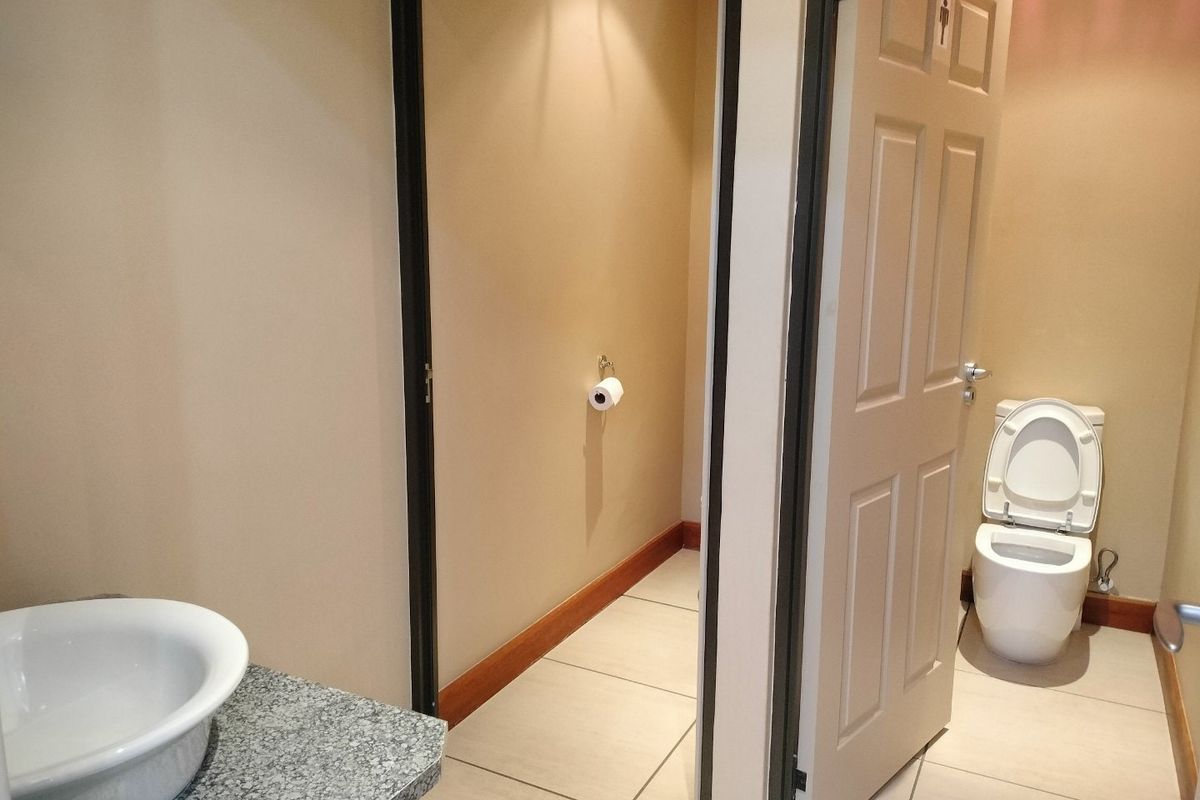 A commercial restroom facility featuring a granite-topped vanity with a vessel sink and a separate enclosed toilet cubicle with tiled flooring.