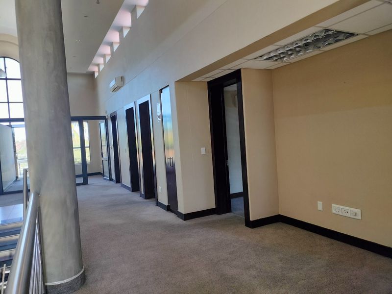 Spacious commercial hallway featuring high ceilings, carpeted flooring, and multiple access points to individual office spaces.