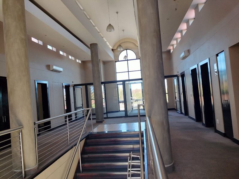 Spacious commercial entrance hall featuring high ceilings, concrete columns, a central staircase with stainless steel balustrades, and large arched windows.