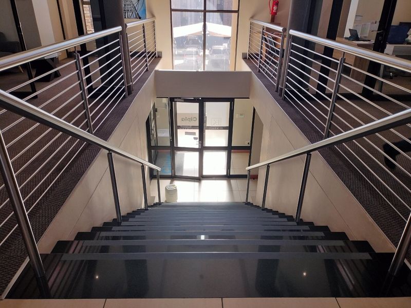 A modern commercial entrance featuring a central staircase with stainless steel balustrades, leading to a glass-fronted main entry door with tiled and carpeted flooring.
