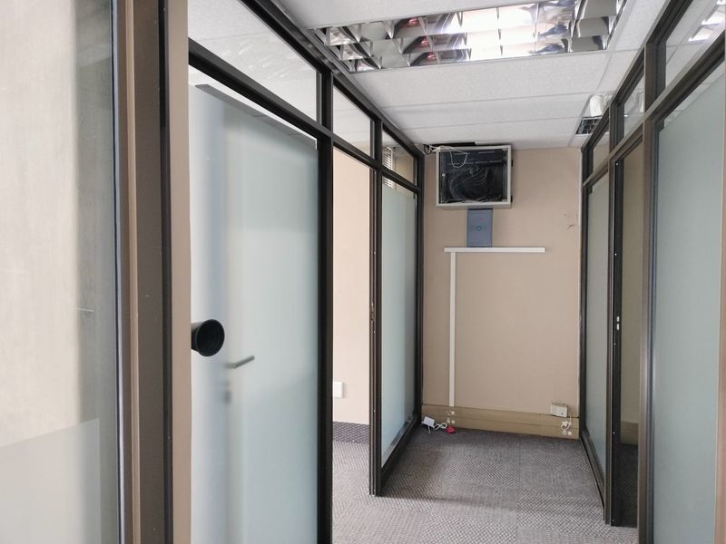 A vacant office space featuring frosted glass partitions, aluminum framing, carpeted flooring, and a suspended ceiling with integrated lighting.