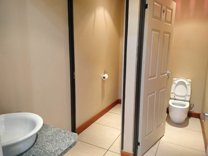 A clean commercial restroom featuring a vessel sink with a granite vanity top and a separate toilet cubicle with tiled flooring.