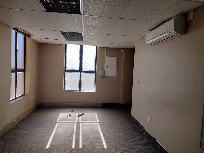 An empty commercial office space featuring a suspended ceiling, split-system air conditioning, and carpeted flooring with natural light from large windows.