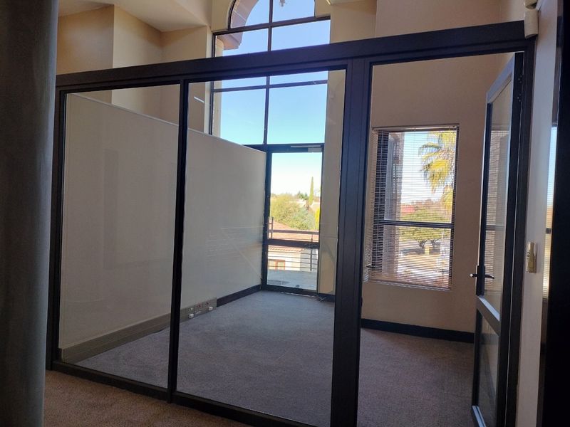 A bright, empty office space featuring modern glass partitioning, high ceilings, and carpeted flooring, offering a professional environment with natural light.