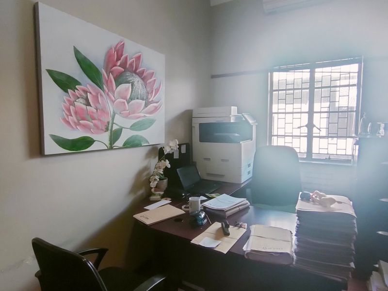 A functional office space featuring a wall-mounted air conditioning unit, security bars on the window, and laminate flooring.