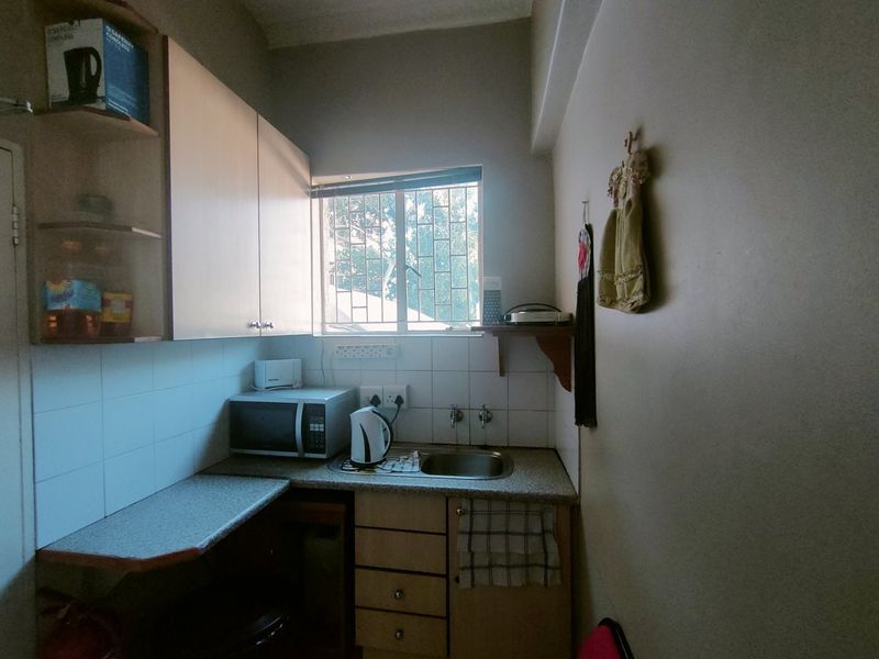 Compact scullery area featuring built-in cabinetry, a stainless steel sink, tiled splashback, and a window providing natural light.
