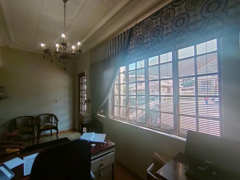 A professional office space featuring ornate ceiling detailing, a classic chandelier, and large windows with fitted blinds providing natural light.
