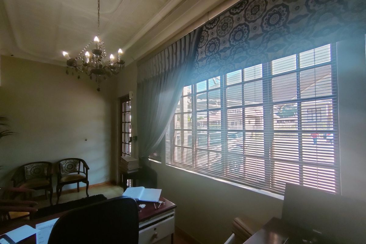 A professional office space featuring ornate ceiling detailing, a classic chandelier, and large windows with fitted blinds providing natural light.