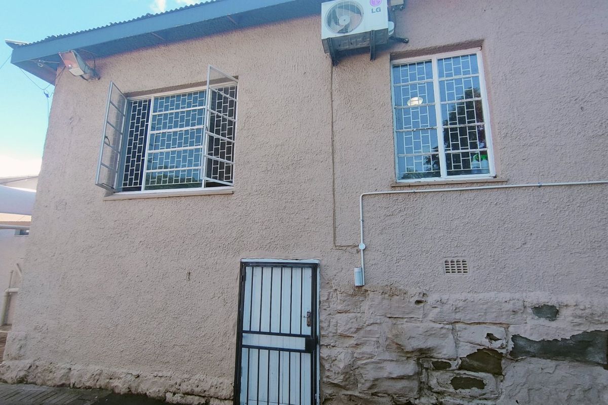 Exterior view of a commercial building featuring security-barred windows, a metal security door, and an external air conditioning unit.