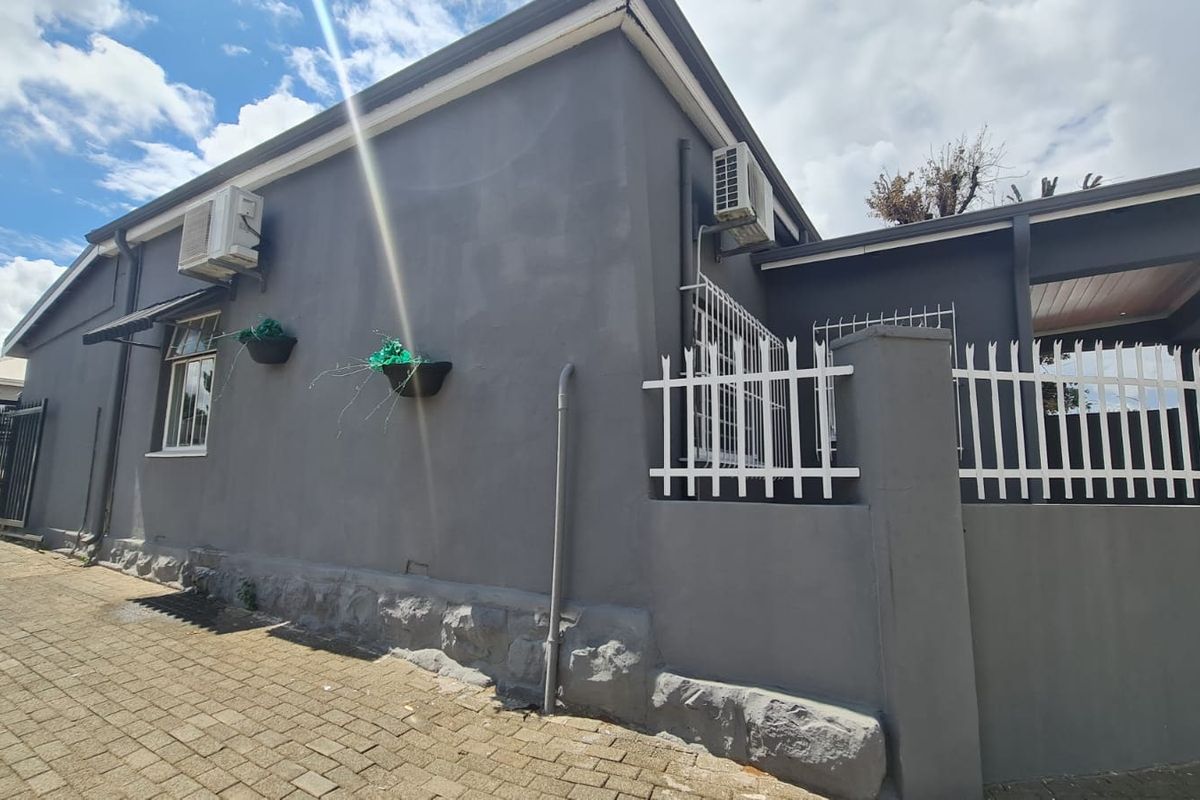 Side exterior view of a commercial property featuring grey painted masonry walls, security fencing, and wall-mounted air conditioning units.