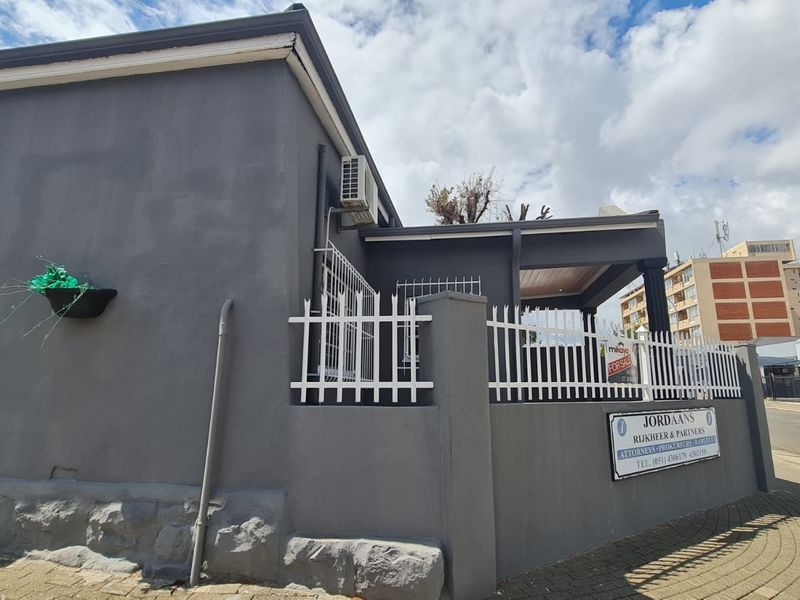 Exterior view of a commercial property featuring a perimeter wall, security fencing, and a covered entrance area with paved surroundings.