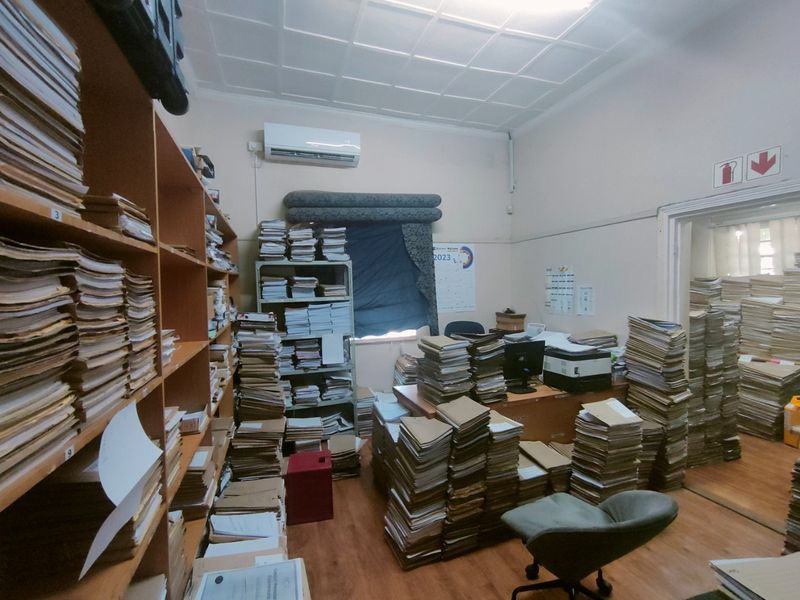 A functional office space featuring built-in shelving, laminate flooring, and a wall-mounted air conditioning unit, currently utilized for document storage.