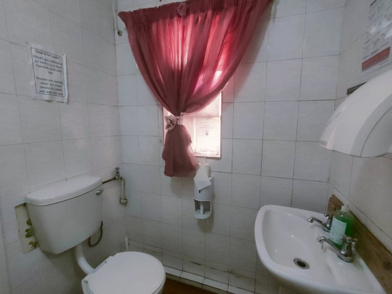 A functional commercial bathroom featuring tiled walls, a standard toilet, and a wall-mounted washbasin with basic fixtures.