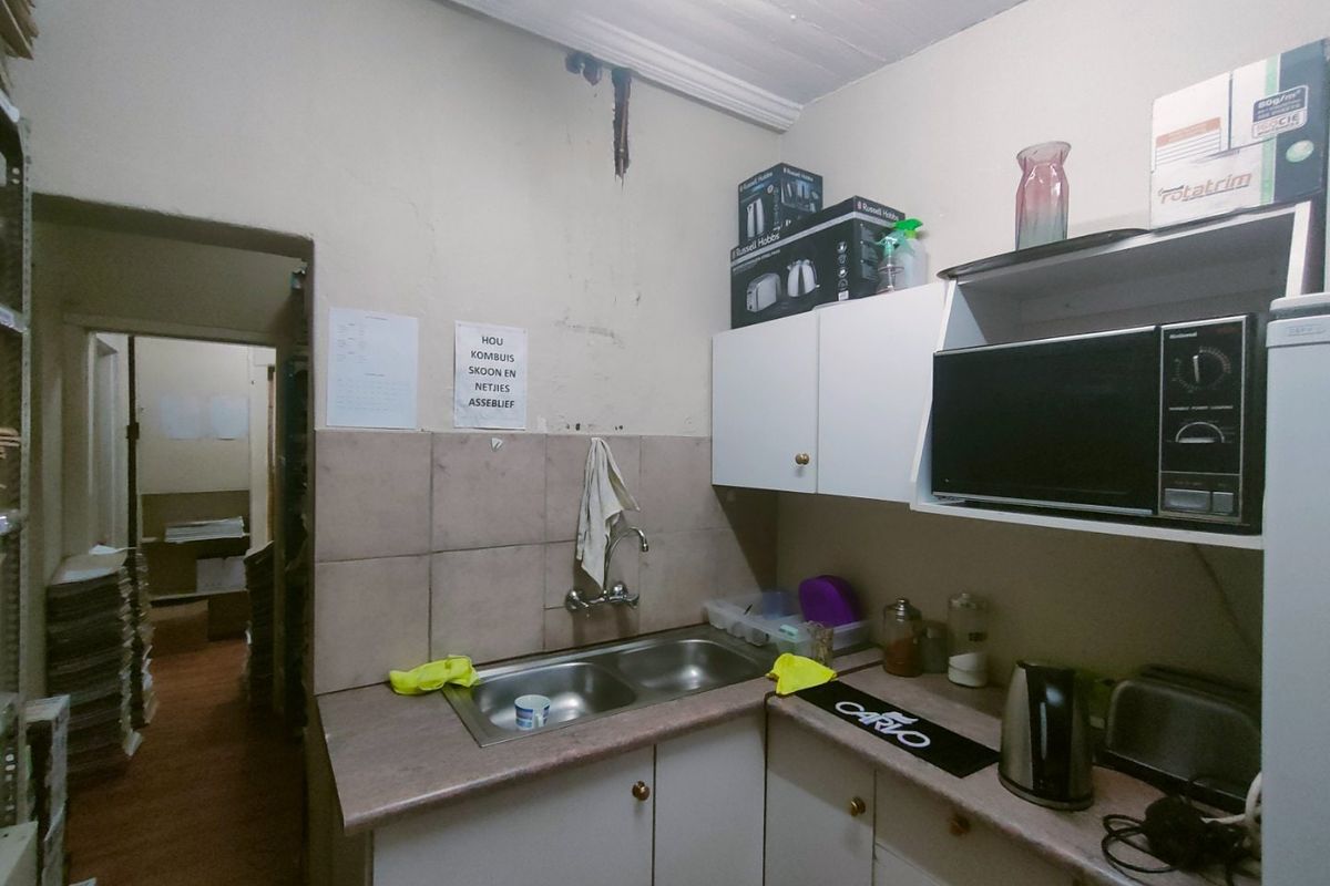 A compact commercial kitchenette featuring a double bowl sink, laminate countertops, and built-in cabinetry, showing signs of wear and water damage on the walls.