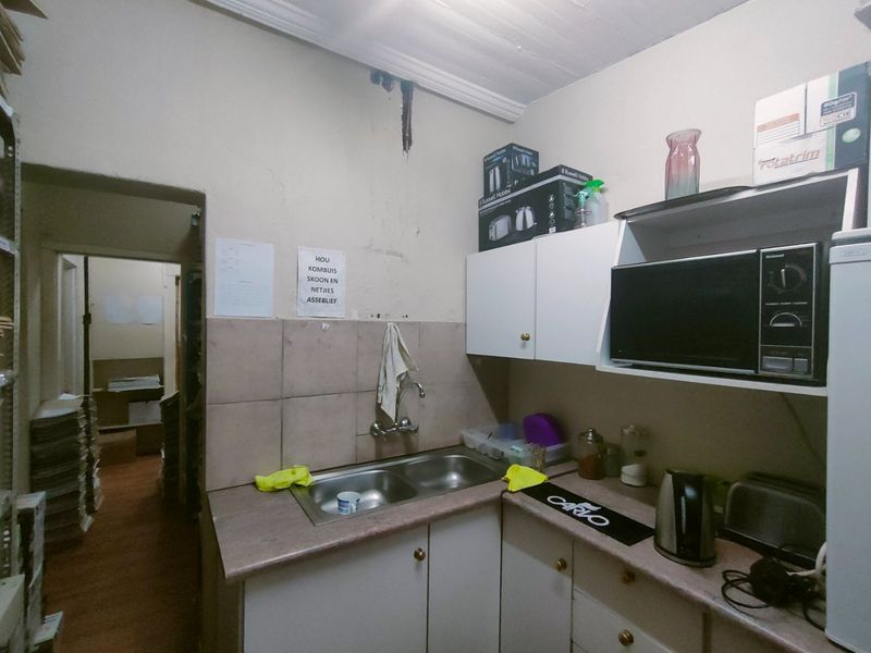 A compact commercial kitchenette featuring a double bowl sink, laminate countertops, and built-in cabinetry, showing signs of wear and water damage on the walls.
