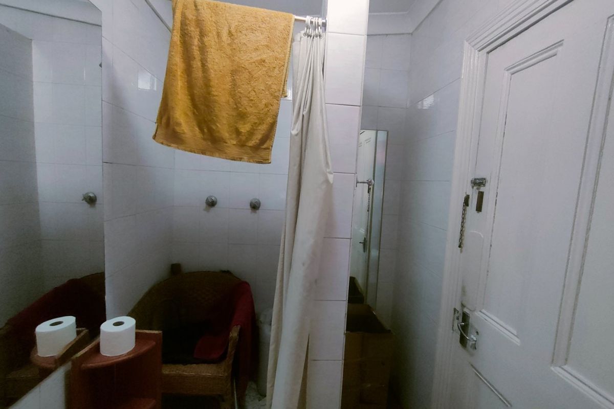 A compact bathroom featuring tiled walls, a shower area with a curtain, and a wall-mounted mirror. The space requires cosmetic updates to improve functionality.