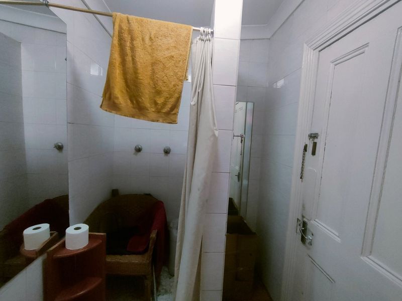 A compact bathroom featuring tiled walls, a shower area with a curtain, and a wall-mounted mirror. The space requires cosmetic updates to improve functionality.