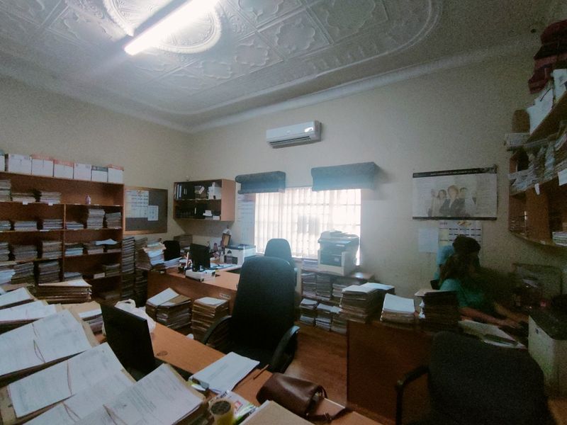 A functional commercial office space featuring timber flooring, built-in shelving units, and an ornate plaster ceiling with a wall-mounted air conditioning unit.