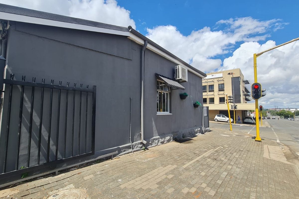 Exterior street-level view of a commercial property featuring a grey facade, security gate, and sidewalk access in a busy urban location.
