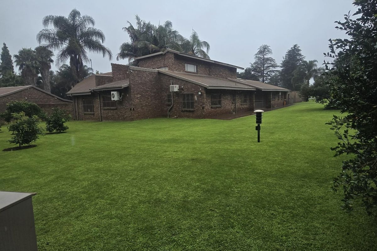 A view of the rear brick farmhouse elevation featuring a well-maintained lawn and established garden surroundings.