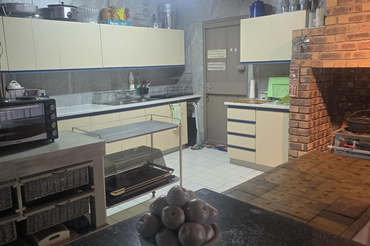 A rustic kitchen featuring built-in cabinetry, granite countertops, a large brick fireplace, and timber ceiling finishes, offering a warm and functional farm-style cooking space.
