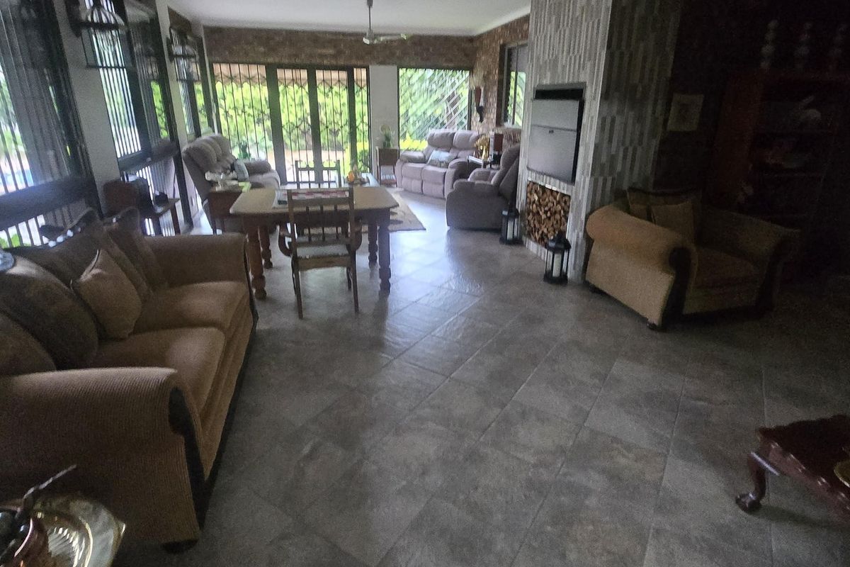 Spacious living area featuring tiled flooring, a built-in fireplace with stone-look cladding, and large windows with security gates.
