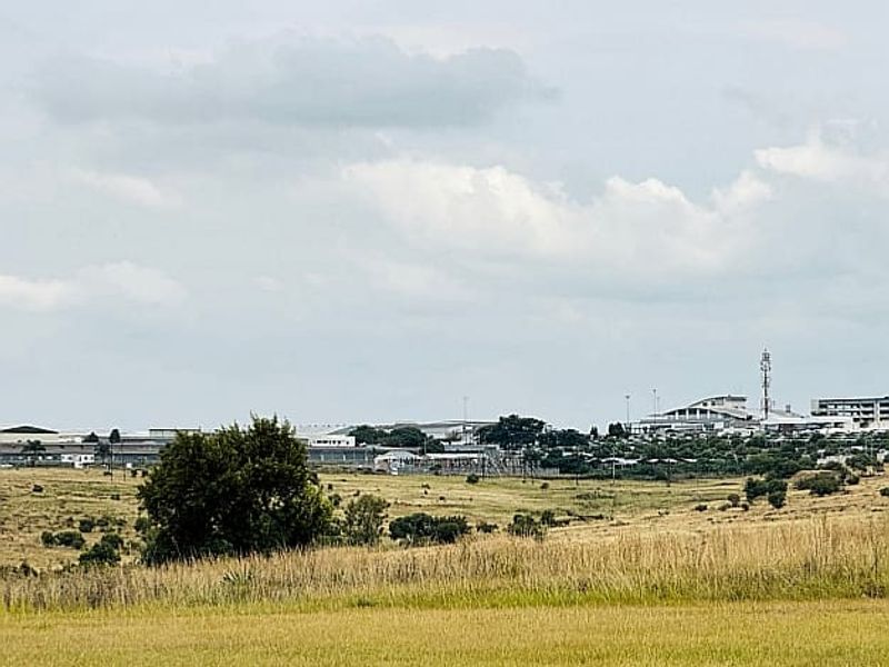 A distant view of a commercial or industrial area featuring large warehouse structures and a telecommunications tower set against a natural landscape.