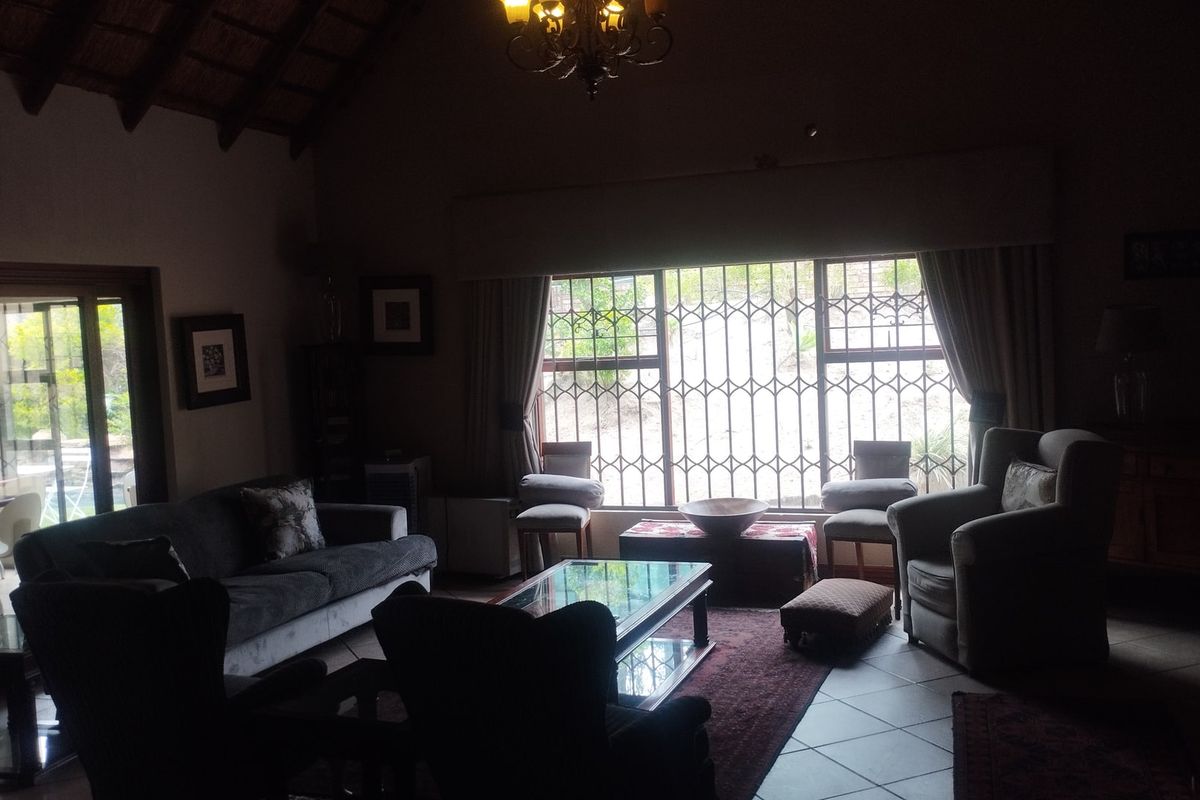 Spacious living room featuring a high vaulted ceiling with exposed timber rafters, tiled flooring, and large windows fitted with security bars.
