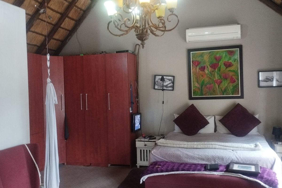 Spacious bedroom featuring a unique thatched roof ceiling, built-in wooden cupboards, and a wall-mounted air conditioning unit.