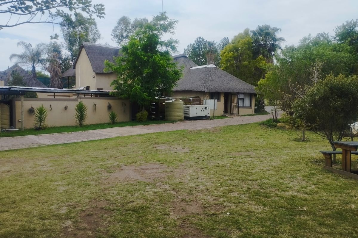Rear view of the commercial property featuring thatch roof buildings, paved driveway, water storage tanks, and a generator set within a landscaped garden area.