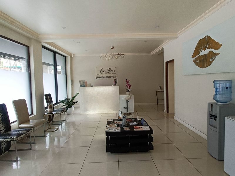 A bright and professional medical reception area featuring tiled flooring, a built-in reception desk, and large windows with privacy film.