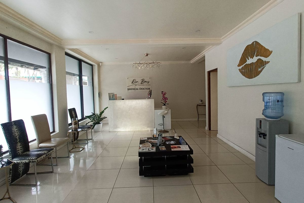 A bright and professional medical reception area featuring tiled flooring, a built-in reception desk, and large windows with privacy film.