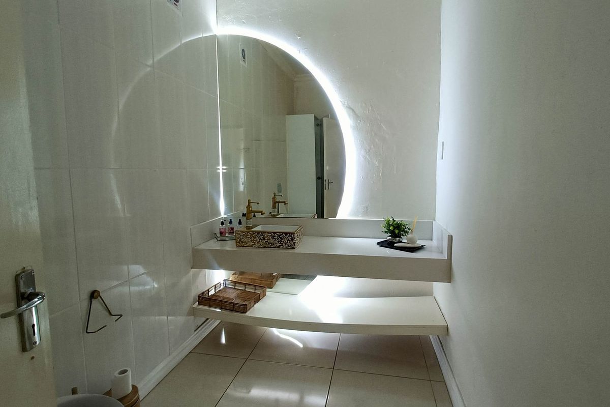 Modern bathroom featuring a floating vanity, vessel sink, and a striking backlit circular mirror with clean tiled finishes.