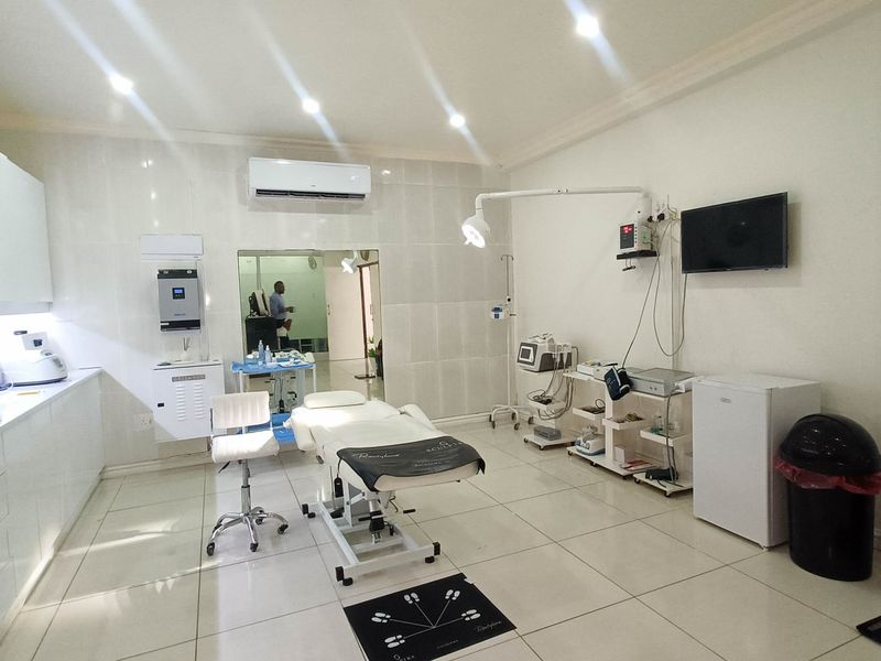 A well-maintained commercial treatment room featuring tiled flooring, built-in cabinetry, wall-mounted air conditioning, and professional medical examination lighting.